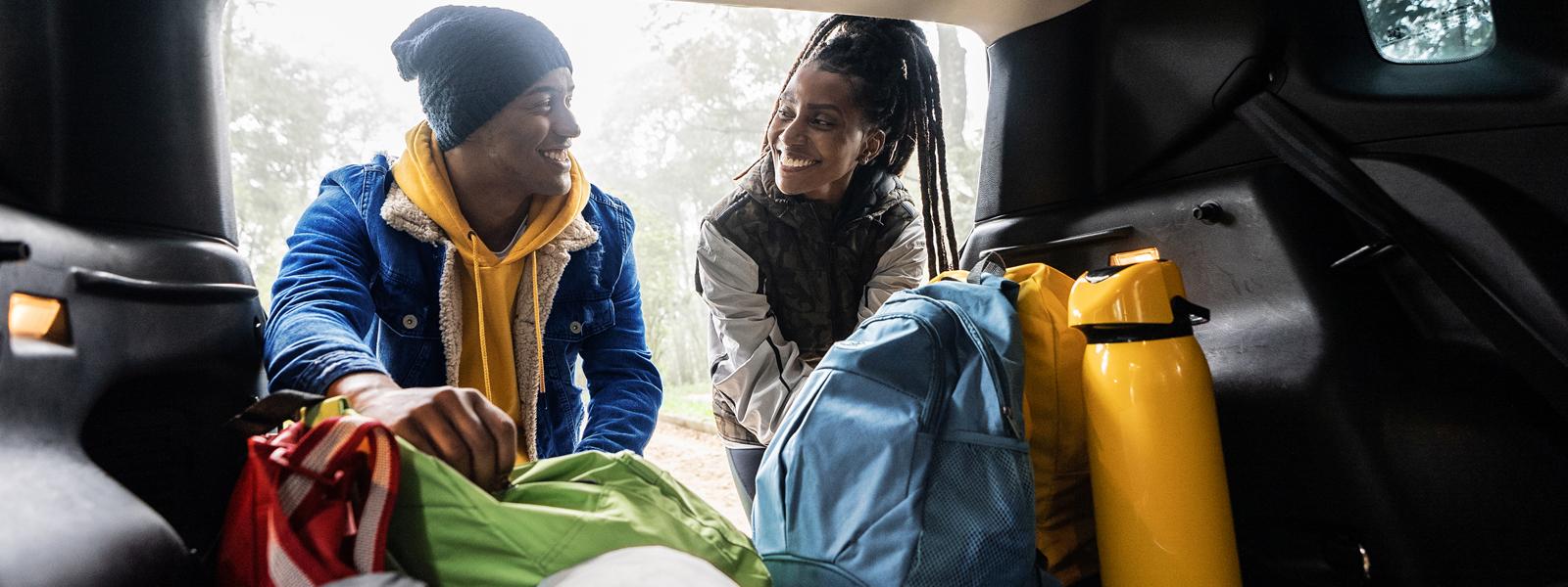 Two people smiling and taking out backpacks from the car.