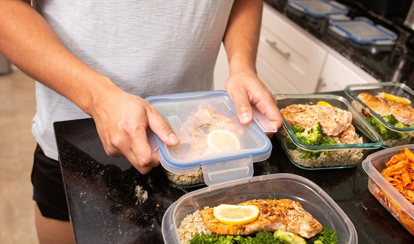 Someone closing the lid on a meal prep container, with three other meals ready to be sealed.
