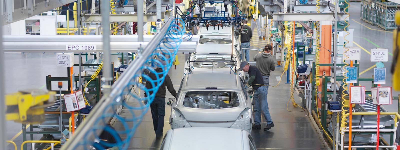 An overhead view of a car assembly plant, where several people work on the cars on the line.