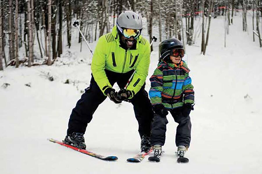 An adult skier assists a young child in learning to ski on a snowy slope.