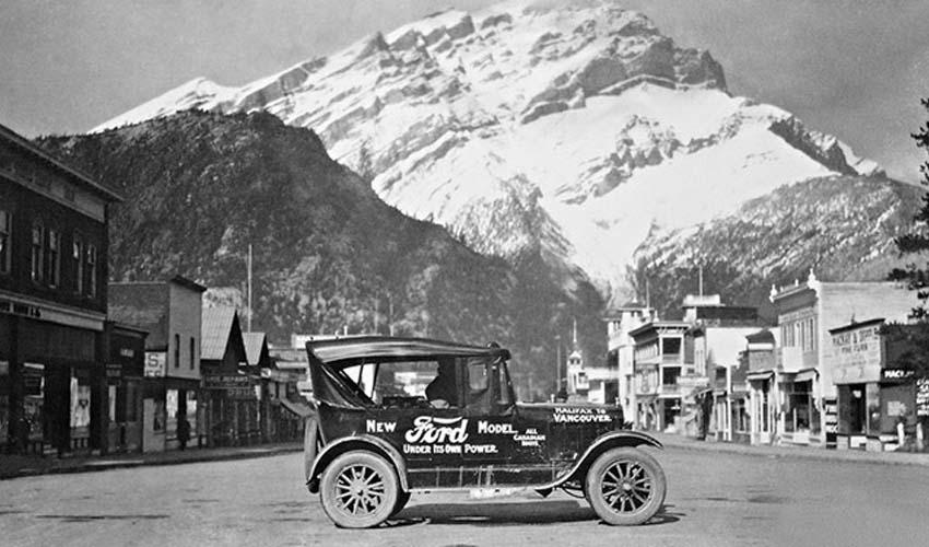 A vintage photo of a car in front of a mountain.