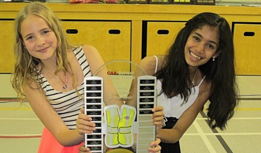Two girls holding up a tennis trophy in a gymnasium.