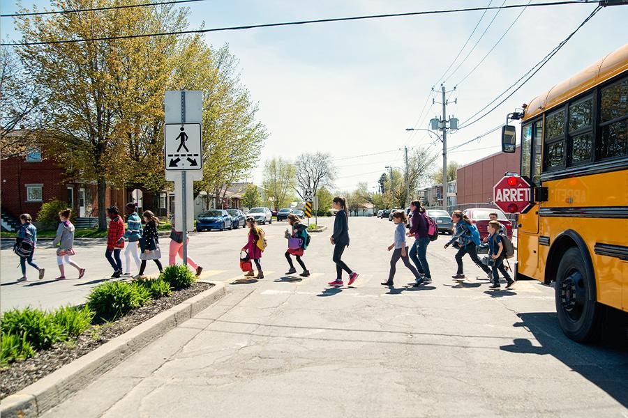 A group of children crossing a street in front of a school bus.