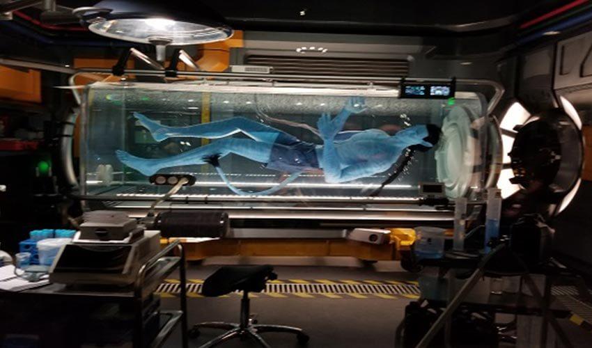 A man is laying in a glass tank in a studio.
