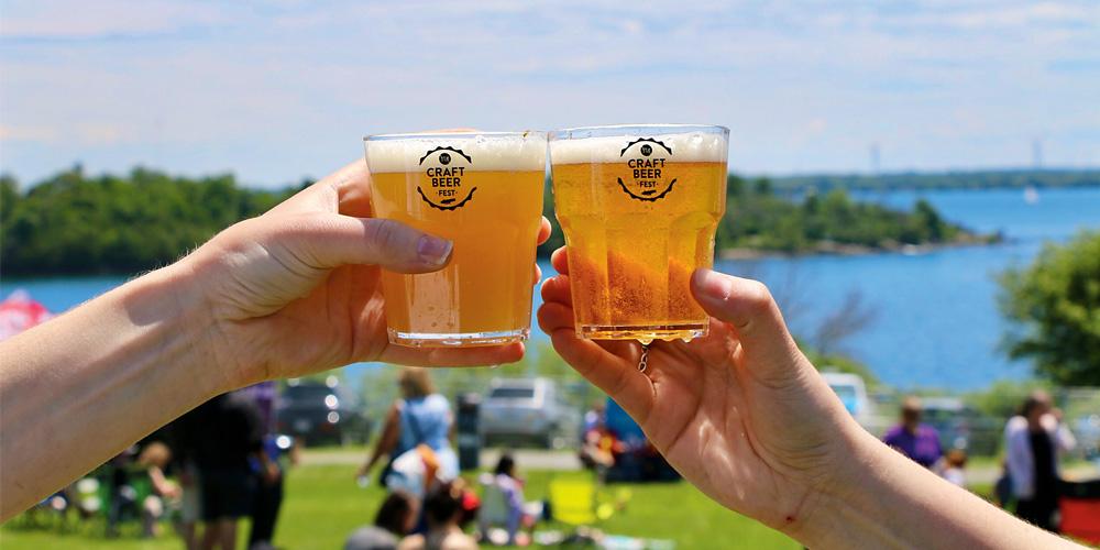 Two people toasting their beer glasses in front of a lake.