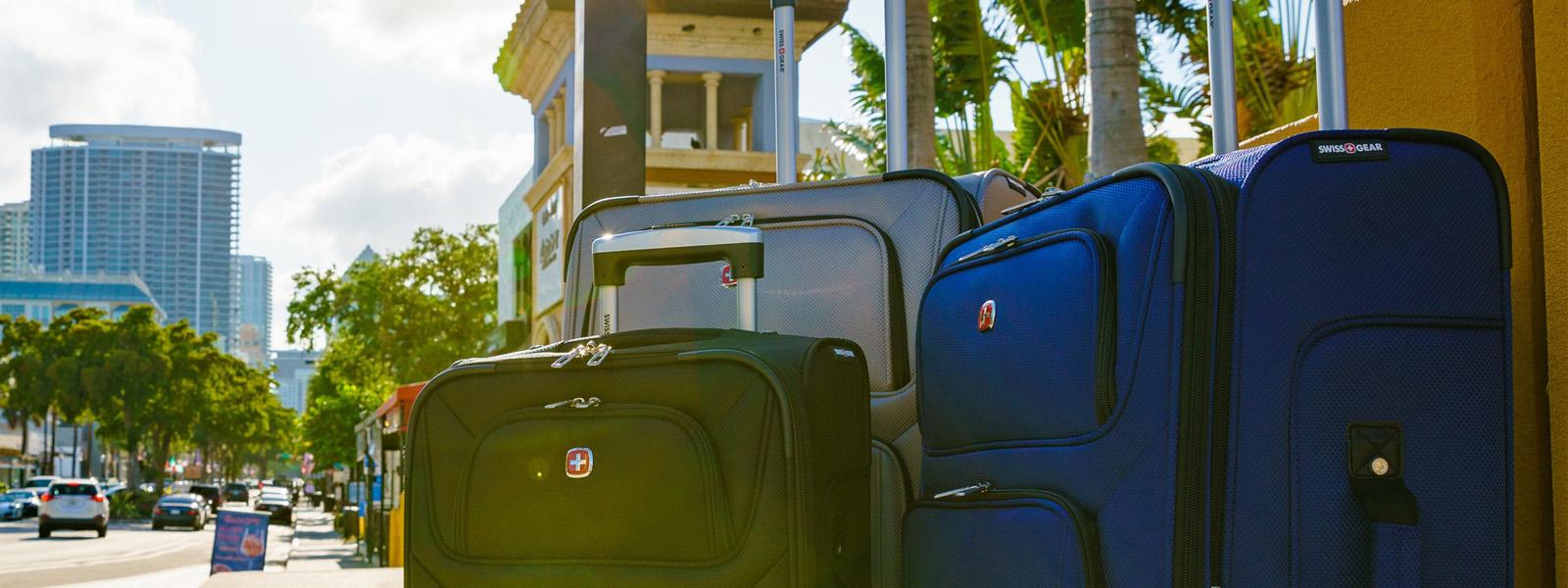 A close-up photograph of multicoloured suitcases standing together on a city sidewalk.